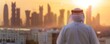 Un homme arabe vêtu d'un kandora blanc regardant au loin les gratte-ciel d'une ville, au coucher du soleil.