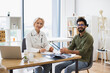 © sofiko14 - Portrait of happy female senior doctor and young male patient sitting at table with portable computer in modern medical office and smiling at camera.