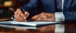© MD Media - A businessman writing in his notebook with a pen at a wooden table in his office. Close up business view