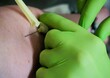 Hände von Ärztin mit grünen Gummihandschuhen stechen Injektionsnadel in Arm von Patientin zur Blutabnahme in Arztpraxis 