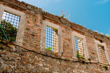 Wall Mural - An ancient wall made of stone with windows that are covered with bars. A fragment of an ancient building with windows and bars on them.