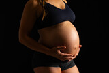 Fototapeta Sawanna - Pregnant Woman Embracing Her Belly on Black Background