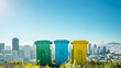 
three colorful recycling bins placed against a cityscape under a clear sky. Each bin corresponds to a different type of recyclable material