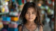 children of cambodia, A portrait of a young girl with tousled hair and a gaze that conveys innocence, set against a colorful blurred background of a market environment. 