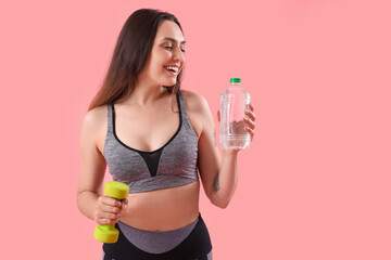 Wall Mural - Sporty young woman with bottle of water and dumbbell on pink background