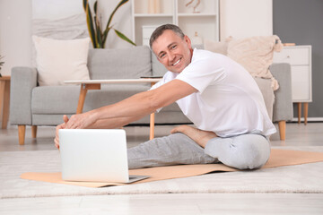 Sticker - Mature man with laptop doing yoga on mat at home