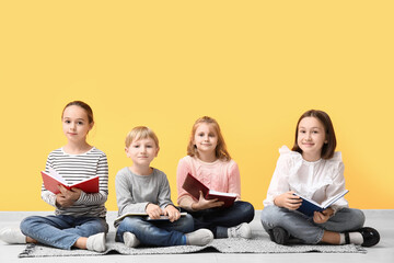 Poster - Little children reading books while sitting on floor near yellow wall