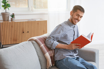 Wall Mural - Young man reading book on sofa at home