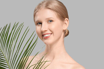 Wall Mural - Young blonde woman with palm leaf on grey background, closeup