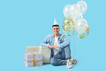 Sticker - Young man with gift boxes and bunch of balloons on blue background