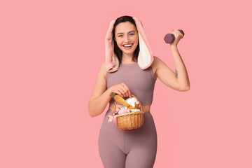 Poster - Happy female fitness coach in bunny ears with Easter basket and dumbbell on pink background