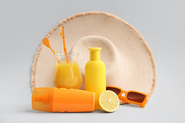 Bottles of sunscreen cream, glass of juice, lemon, sunglasses and hat on white background