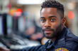 A young African American officer with a hopeful smile works in a control room, his demeanor reflecting the positive relationship between law enforcement and the community in the glow of duty.