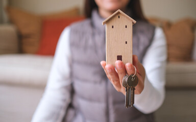 Wall Mural - Closeup image of a woman holding a wooden house model and the keys for real estate concept