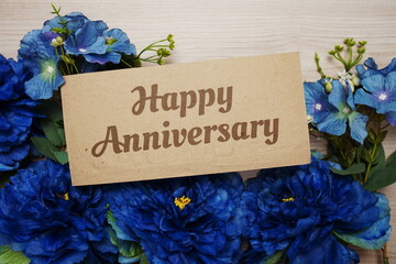 Sticker - Happy Anniversary text message on paper card with flowers border frame on wooden background