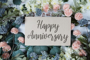 Sticker - Happy Anniversary text message on paper card with flowers border frame on wooden background