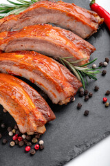 Wall Mural - A portion of barbecue pork ribs cut into pieces in BBQ sauce on a black slate board on a white background with seasonings and pepper, close up