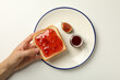 © Atlas - Fig jam, plate and toaster bread in hand on white background, top view