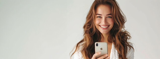 Wall Mural - Photo of An elegant woman in her 20s with long wavey hair, smiling while using smartphone on a white background with copy space for text or product. Web banner. Mobile phone use