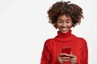 © MD Media - Portrait of smiling happy african american woman using smartphone isolated on white background, wearing red sweater with copy space for text or promotion banner.