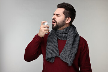 Canvas Print - Young man with scarf using throat spray on grey background