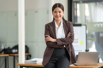 Asian businesswoman smiling confidently. A successful entrepreneur in the financial business professional company executive wearing a suit standing with arms crossed in the office.