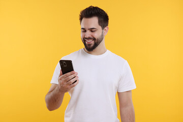 Canvas Print - Happy young man using smartphone on yellow background