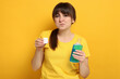 © New Africa - Young woman using mouthwash on yellow background