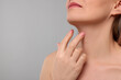 Woman touching her neck on grey background, closeup. Space for text