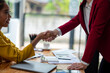 © apichat - Close-up of two businesswomen shaking hands over a desk, symbolizing a successful agreement or partnership in a professional setting.