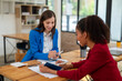 © apichat - Two professional women in a lively discussion at an office desk, with one in a yellow blazer gesturing and the other showing surprise.