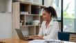 © apichat - Confident female entrepreneur conducting financial analysis on her laptop in a well-lit office space.