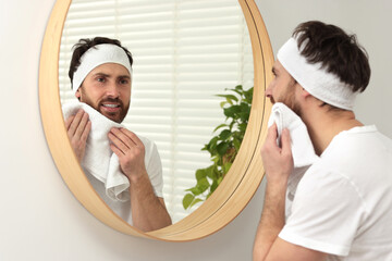 Canvas Print - Washing face. Man with headband and towel near mirror in bathroom