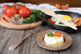 Fototapeta Koty - On a wooden table is a plate with fried egg, tomato and greens.
