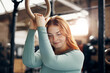 © Flamingo Images - Young red head woman smiling while exercising on rings at the gym. Sunlight shines through the windows behind her