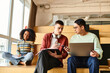 © LIGHTFIELD STUDIOS - Three individuals of different ethnicities sitting on a bench, focused on a laptop screen