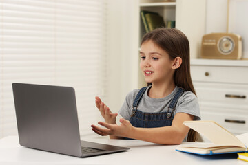 Wall Mural - Cute girl having online lesson at white table indoors