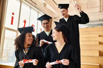 Wall Mural - A group of diverse students in graduation gowns holding diplomas, smiling in celebration of their academic accomplishments.