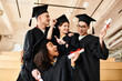 © LIGHTFIELD STUDIOS - A diverse group of happy students in graduation gowns and academic caps posing for a picture indoors.