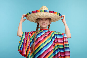 Wall Mural - Cute girl in Mexican sombrero hat and poncho on light blue background
