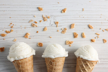 Wall Mural - Ice cream scoops in wafer cones on light wooden table, flat lay