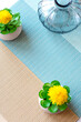 two green artificial decors and glass container on a brown and blue striped tablecloth. Free place for text and logo