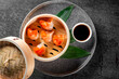 An intriguing Asian cuisine setting with a bamboo steamer, green leaves, and a cup of sauce on a textured surface, main dish obscured