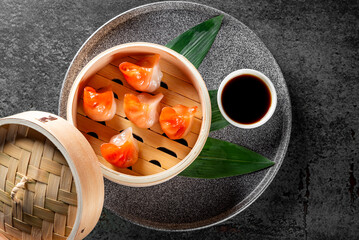 Wall Mural - An intriguing Asian cuisine setting with a bamboo steamer, green leaves, and a cup of sauce on a textured surface, main dish obscured