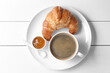 Fresh croissant, jam and coffee on white wooden table, top view. Tasty breakfast