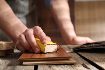 Wall Mural - Man polishing wooden plank with sandpaper at table indoors, closeup