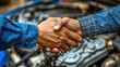 Two men shake hands in front of a car engine