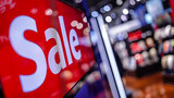 Fototapeta  - Close Up of a Red Sale Sign in a Home Electronics Department Store with a Range of Modern Smart TV Sets. Shoppers Explore Discounted Home Appliances in a Busy Retail Storefront