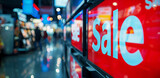 Fototapeta  - Close Up of a Red Sale Sign in a Home Electronics Department Store with a Range of Modern Smart TV Sets. Shoppers Explore Discounted Home Appliances in a Busy Retail Storefront