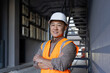 © Tetiana - Portrait of a smiling Asian male engineer, construction worker, technician standing outside a building in a hard hat and vest, crossing his arms over his chest and looking confidently at the camera